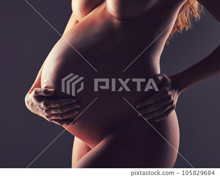 Pregnant woman, naked in studio with hand on stomach and aesthetic dark background at maternity reveal. Creative pregnancy photoshoot, art and nude mother holding belly with healthy body and wellness 105829684