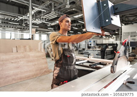 Young carpenter cutting a piece of wood in using a circular saw in furniture factory Young carpenter cutting a piece of wood in using a circular saw in furniture factory 105829775