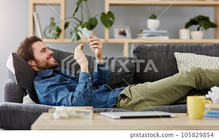Social networking, man with smartphone on sofa and lying in living room at his home. Connectivity or technology, smile and happy male person with cellphone comfortable on couch playing online game Social networking, man with smartphone on sofa and lying in living room at his home. Connectivity or technology, smile and happy male person with cellphone comfortable on couch playing online game 105829854