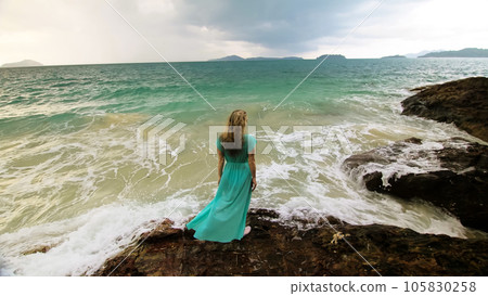 Woman walks on rock of sea reef stone, stormy cloudy ocean. Blue swimsuit dress tunic. Concept rest, tropical resort coastline tourism summer holidays 105830258