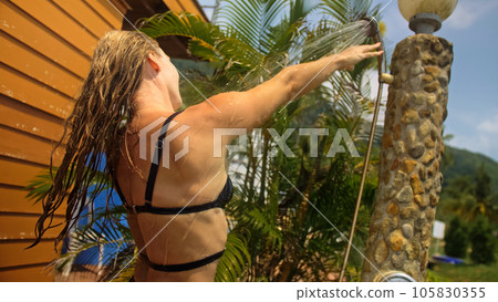 Woman taking a shower in garden near hotel. Girl washes hair, er 105830355