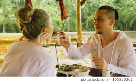 Man and woman eat and drink tasty beverages spending time in traditional local floating cafe on water. Loving happy couple having breakfast outdoors Man and woman eat and drink tasty beverages spending time in traditional local floating cafe on water. Loving happy couple having breakfast outdoors 105830361