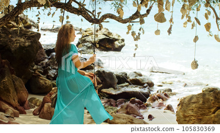 Pretty woman swinging on a swing on a tropical beach, on shores of the turquoise sea. Concept travel, walks, rest in sea, tropical resort coastline relaxation traveling tourism summer holidays. 105830369
