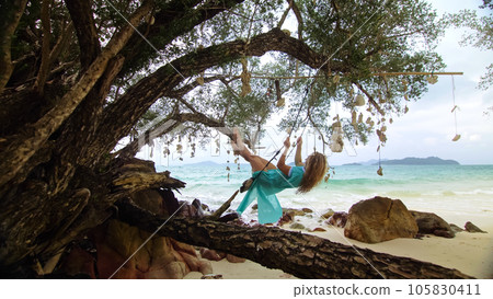 Pretty woman swinging on a swing on a tropical beach, on shores of the turquoise sea. Concept travel, walks, rest in sea, tropical resort coastline relaxation traveling tourism summer holidays. Pretty woman swinging on a swing on a tropical beach, on shores of the turquoise sea. Concept travel, walks, rest in sea, tropical resort coastline relaxation traveling tourism summer holidays. 105830411