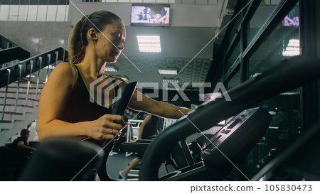 Fit Athletic Woman Exercising on an Elliptical Machine. Muscular Women Activity Training in Modern Gym. Workout in an Elliptic Walking Trainer. Fit Athletic Woman Exercising on an Elliptical Machine. Muscular Women Activity Training in Modern Gym. Workout in an Elliptic Walking Trainer. 105830473