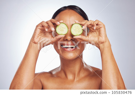 Cucumber, face and natural beauty of happy woman in studio, white background and healthy diet. Female model, skincare and fruits on eyes for sustainable cosmetics, aesthetic dermatology and nutrition Cucumber, face and natural beauty of happy woman in studio, white background and healthy diet. Female model, skincare and fruits on eyes for sustainable cosmetics, aesthetic dermatology and nutrition 105830476