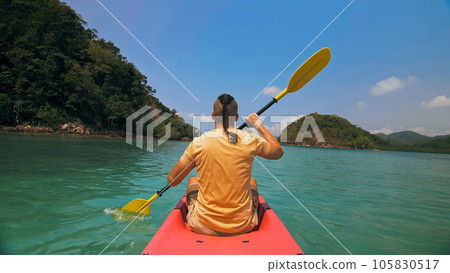 Man with sunglasses and hat rows pink plastic canoe along sea ag 105830517
