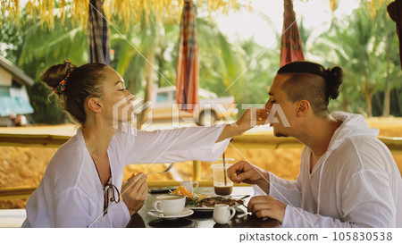 Man and woman eat and drink tasty beverages spending time in traditional local floating cafe on water. Loving happy couple having breakfast outdoors Man and woman eat and drink tasty beverages spending time in traditional local floating cafe on water. Loving happy couple having breakfast outdoors 105830538