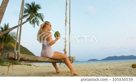 Attractive woman is swinging on a swing. Sexy hot erotic bad girl posing on the beach against the backdrop of the sea. Concept natural beauty body, femininity and sexuality, debauchery and courage. Attractive woman is swinging on a swing. Sexy hot erotic bad girl posing on the beach against the backdrop of the sea. Concept natural beauty body, femininity and sexuality, debauchery and courage. 105830539