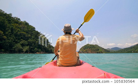 Man with sunglasses and hat rows pink plastic canoe along sea ag Man with sunglasses and hat rows pink plastic canoe along sea ag 105830564