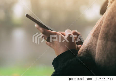 Hands, phone and social media with a person on a blurred background outdoor on an overcast day. Mobile, contact and communication with an adult typing a text message in the rain during winter Hands, phone and social media with a person on a blurred background outdoor on an overcast day. Mobile, contact and communication with an adult typing a text message in the rain during winter 105830655