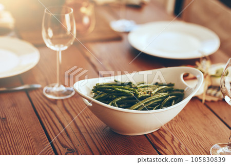 Thanksgiving, green beans and food with a place setting on a dining room table for a celebration event. Party, dish and dinner with a bowl on a wooden surface in celebration or holiday tradition Thanksgiving, green beans and food with a place setting on a dining room table for a celebration event. Party, dish and dinner with a bowl on a wooden surface in celebration or holiday tradition 105830839