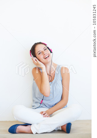 Headphones, music and portrait of woman on a floor in studio, happy and streaming on a wall background. Face, smile and girl relax with podcast, radio or audio track while sitting against mockup 105831245