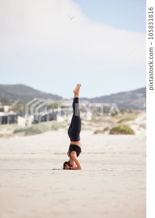 It takes patience to master this pose. a young woman doing a headstand while practising yoga at the beach. 105831816