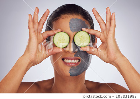 Face, cucumber and mask with a model woman in studio on a gray background for an antiaging facial treatment. Eyes, skincare and fruit with a young female person using cosmetic lay on her face 105831982