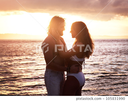 Happy couple, hug and sunset at the beach for love, quality time or bonding together in the water. Man and woman hugging in loving romance, sunrise or sunshine in the ocean for romantic holiday 105831990