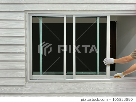Construction worker repairing the sliding window on artificial woods siding. 105833890