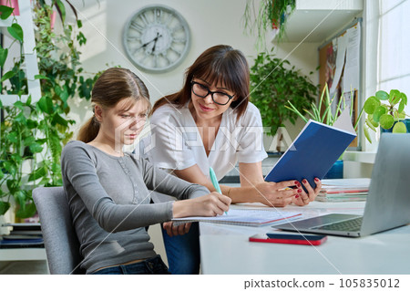 Mother helping preteen daughter to study, looking at laptop at home 105835012