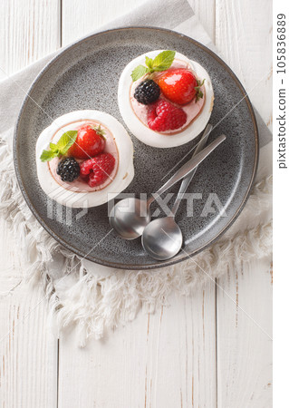 Strawberries, dewberry, raspberries and cream decorates to Anna Pavlova cakes on a plate. Vertical top view 105836889