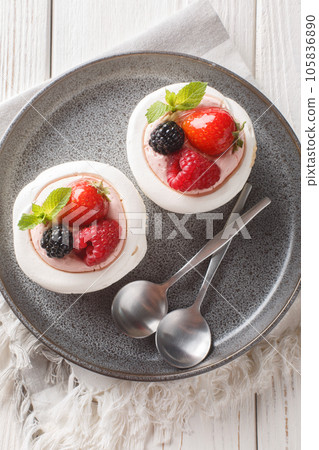Pavlova meringue nest with berries and mint leaves on a plate. Vertical top view 105836890