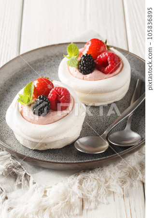 Strawberries, dewberry, raspberries and cream decorates to Anna Pavlova cakes on a plate. Vertical 105836895