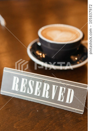 Coffee cup with a heart pattern in a blue cup on a wooden background. A sign with the inscription - reserved. Coffee cup with a heart pattern in a blue cup on a wooden background. A sign with the inscription - reserved. 105837972