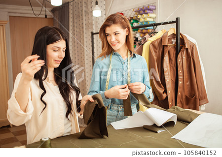 Seamstresses sew fabric by hand, sweep away details of future outfit. Work process, crafting, workplace. smiling, real 105840152