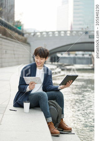 A young man holding a tablet and a map in a park with a river 105840230