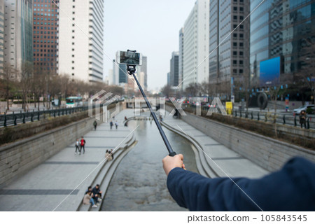 A man's hand holding a camera against a river-flowing city background A man's hand holding a camera against a river-flowing city background 105843545