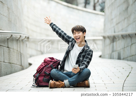 A young man sitting on the street taking pictures with a smartphone camera while traveling 105844217