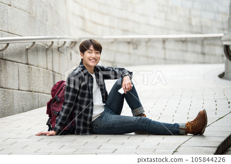 A young man sitting on the street taking pictures with a smartphone camera while traveling 105844226