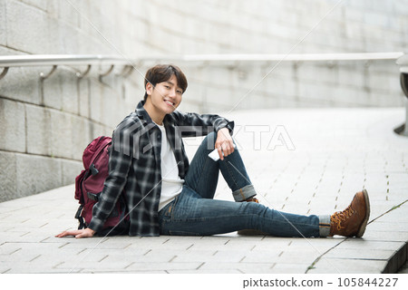 A young man sitting on the street taking pictures with a smartphone camera while traveling 105844227