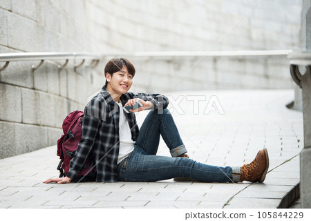 A young man sitting on the street taking pictures with a smartphone camera while traveling 105844229