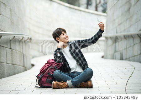 A young man traveling around a traditional village and taking pictures with a smartphone camera A young man traveling around a traditional village and taking pictures with a smartphone camera 105845489