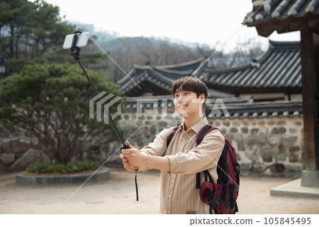 A young man traveling around a traditional village and taking pictures with a smartphone camera A young man traveling around a traditional village and taking pictures with a smartphone camera 105845495
