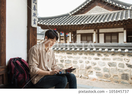 A young man who uses a tablet while traveling in tourist attractions with traditional Korean houses 105845737