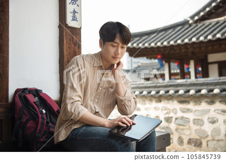 A young man who uses a tablet while traveling in tourist attractions with traditional Korean houses 105845739