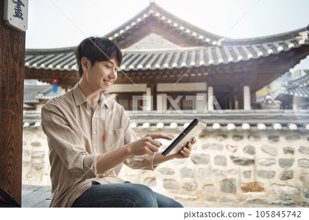A young man who uses a tablet while traveling in tourist attractions with traditional Korean houses A young man who uses a tablet while traveling in tourist attractions with traditional Korean houses 105845742