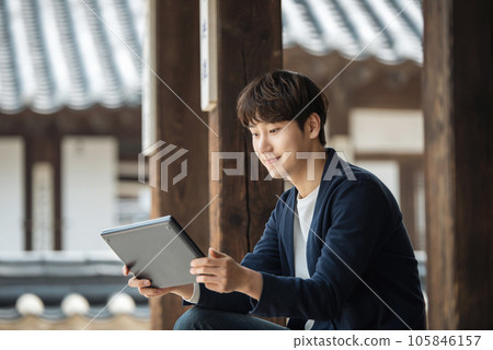 A young male college student sitting and looking at a tablet while traveling in Korea A young male college student sitting and looking at a tablet while traveling in Korea 105846157