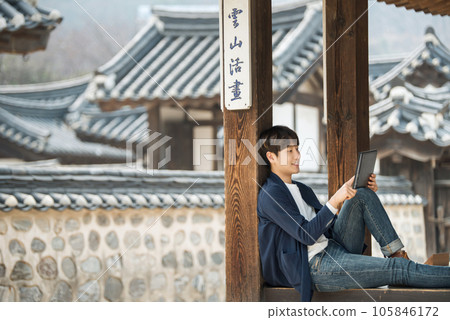 A young male college student sitting and looking at a tablet while traveling in Korea A young male college student sitting and looking at a tablet while traveling in Korea 105846172
