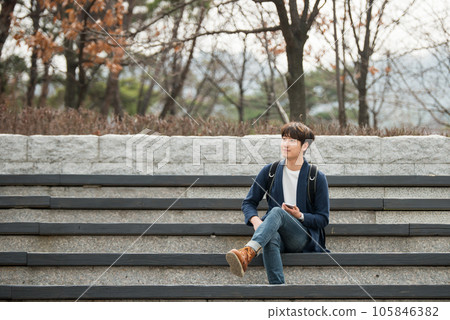 A young man sitting on the stairs looking at his smartphone 105846382