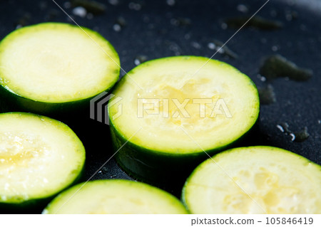 A cooking scene where round slices of zucchini are baked in a frying pan. A cooking scene where round slices of zucchini are baked in a frying pan. 105846419