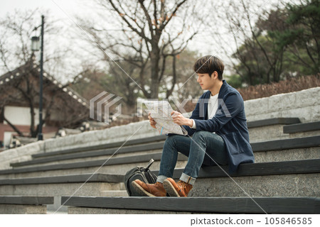 a young man sitting on the stairs looking at a map a young man sitting on the stairs looking at a map 105846585