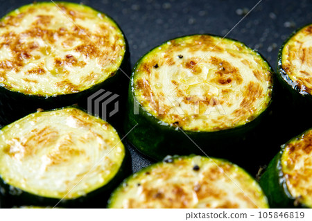 A cooking scene where round slices of zucchini are baked in a frying pan. 105846819