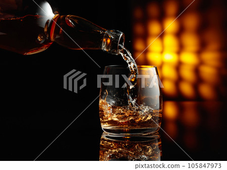 Pouring whiskey from a bottle into a glass. Pouring whiskey from a bottle into a glass. 105847973
