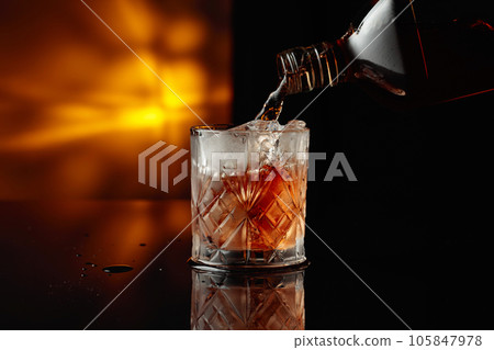 Pouring whiskey from a bottle into a glass with ice. Pouring whiskey from a bottle into a glass with ice. 105847978