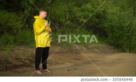 A young man in a yellow raincoat is fishing on the shore. The man caught seaweed on a hook and is crying. 105848446