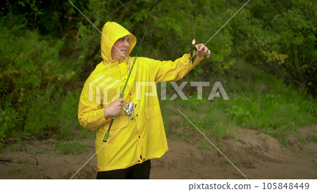 A young man in a yellow cloak with a hood is fishing on the shore. A joyful man caught seaweed on a hook. 105848449