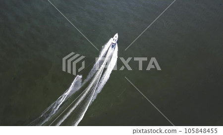 A young man is skiing. A sports guy is skiing on the water behind a boat. Top view from a drone. 105848455