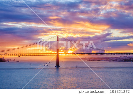 View of 25 de Abril Bridge famous tourist landmark of Lisbon connecting Lisboa and Almada on Setubal Peninsula over Tagus river with tourist yacht boats on sunset. Lisbon, Portugal 105851272